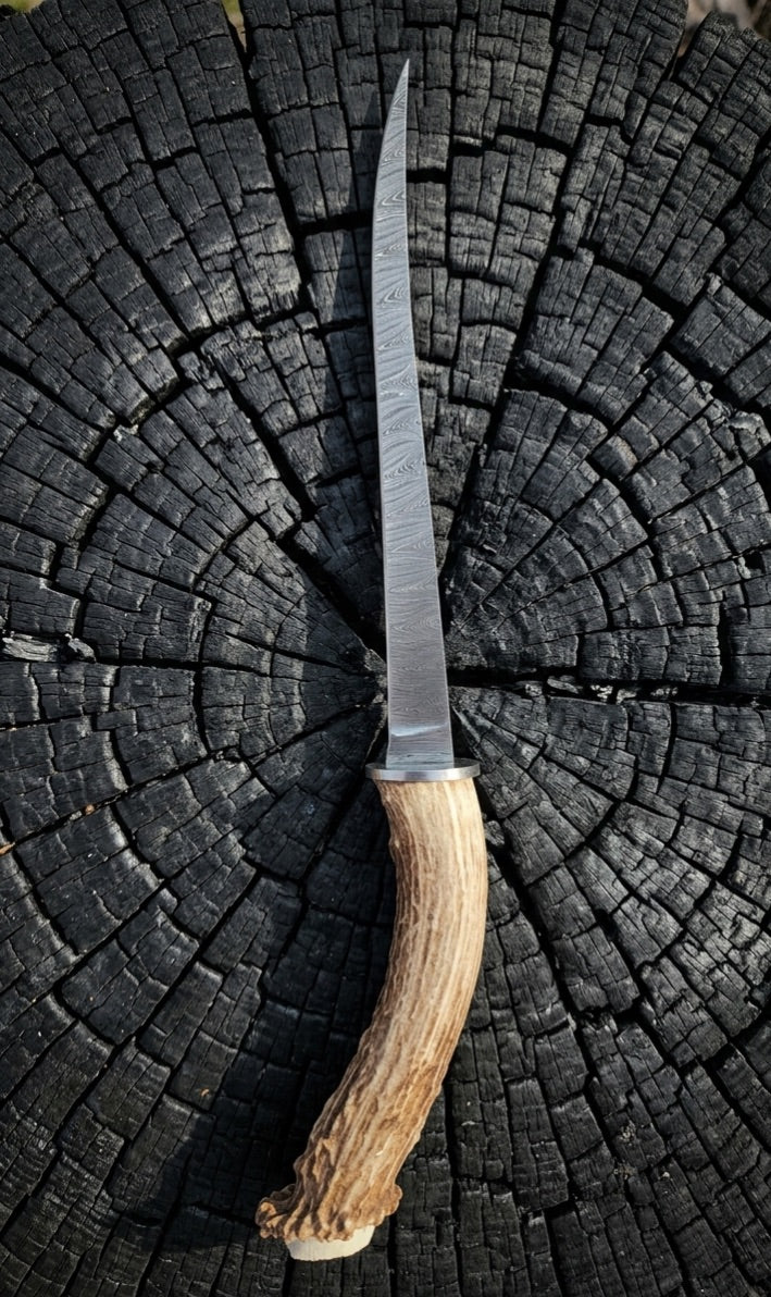 Long damascus knife centered on charred wood